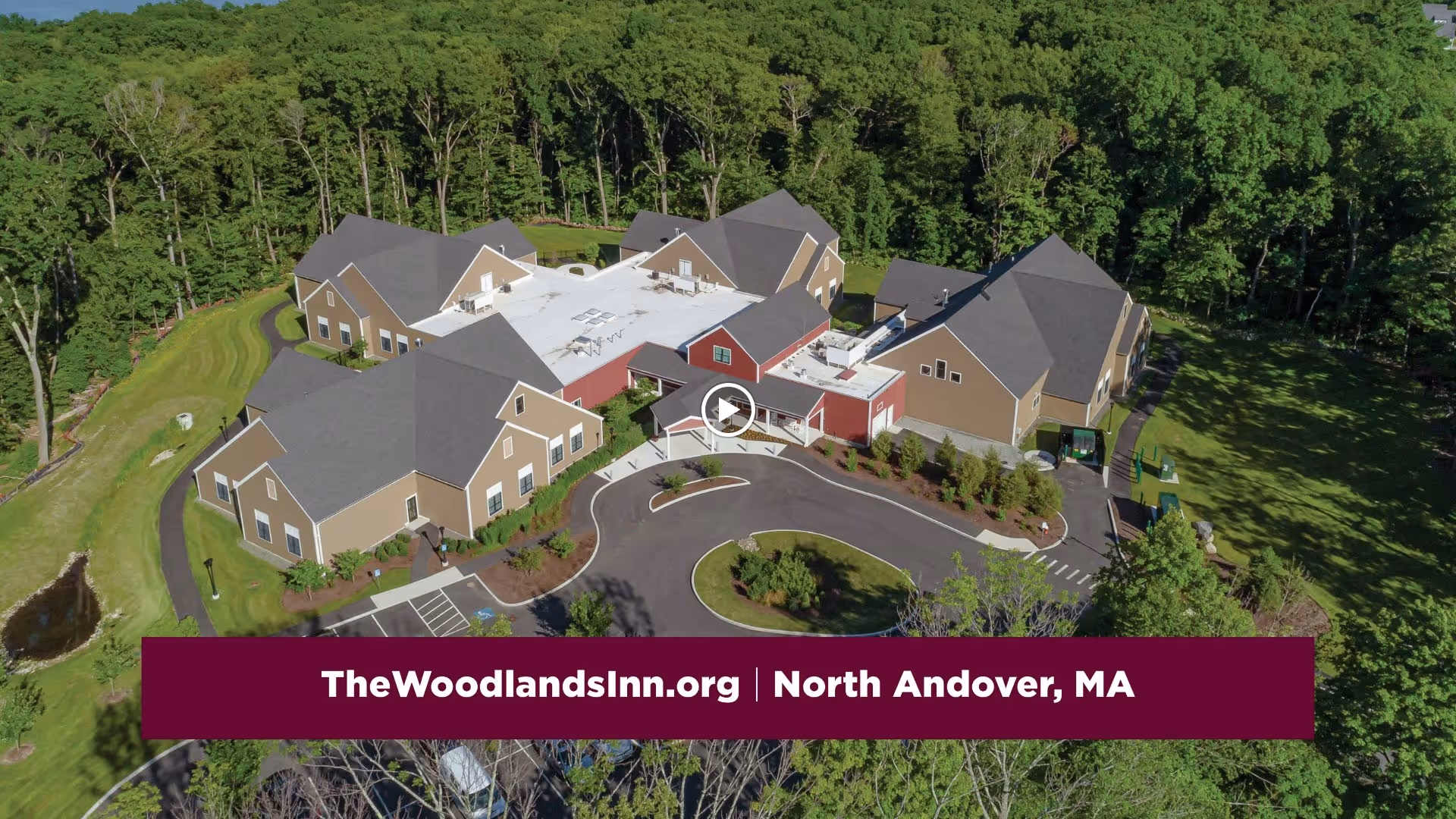 Aerial view of The Woodlands Inn at Edgewood senior living facility surrounded by trees and greenery, showing multiple connected buildings with gray roofs and a circular driveway in front.
