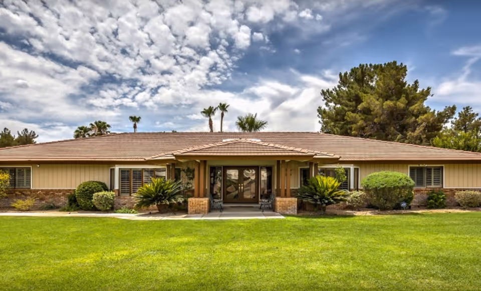 A single-story senior living facility with tan siding, front entrance, and manicured lawn.