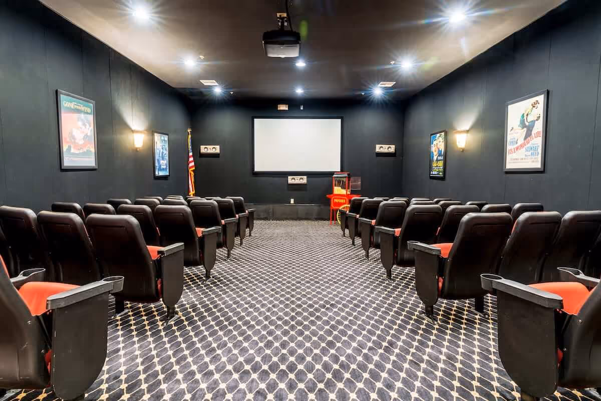Small private movie theater room with rows of black and red seats facing a projection screen and popcorn machine.