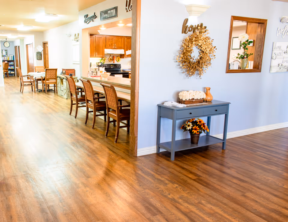 Bright communal dining and kitchen area with bar stools, wooden floors, and a decorative console table with a wreath.