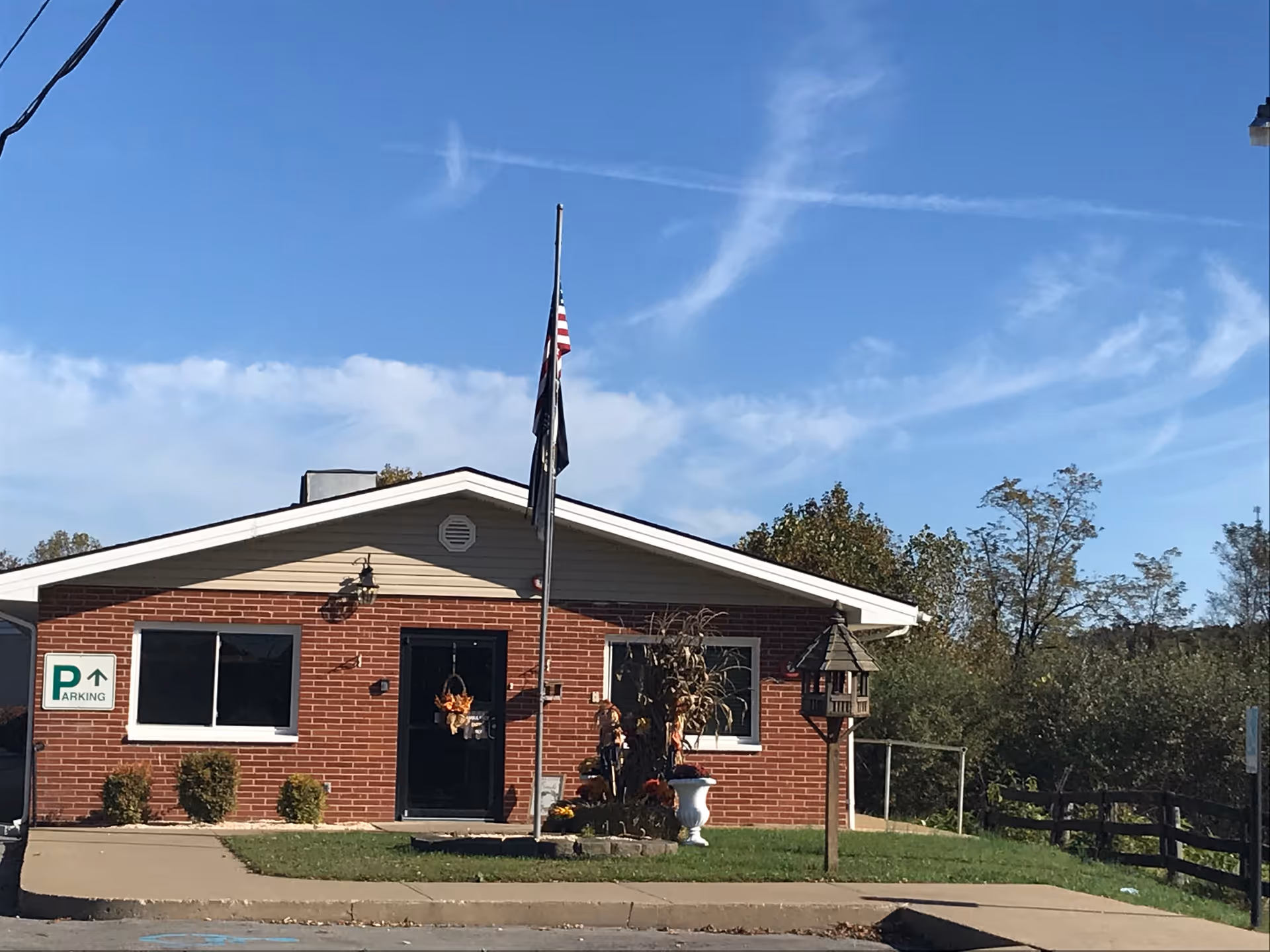 Single-story brick building front with a flagpole, seasonal wreaths and a parking sign.