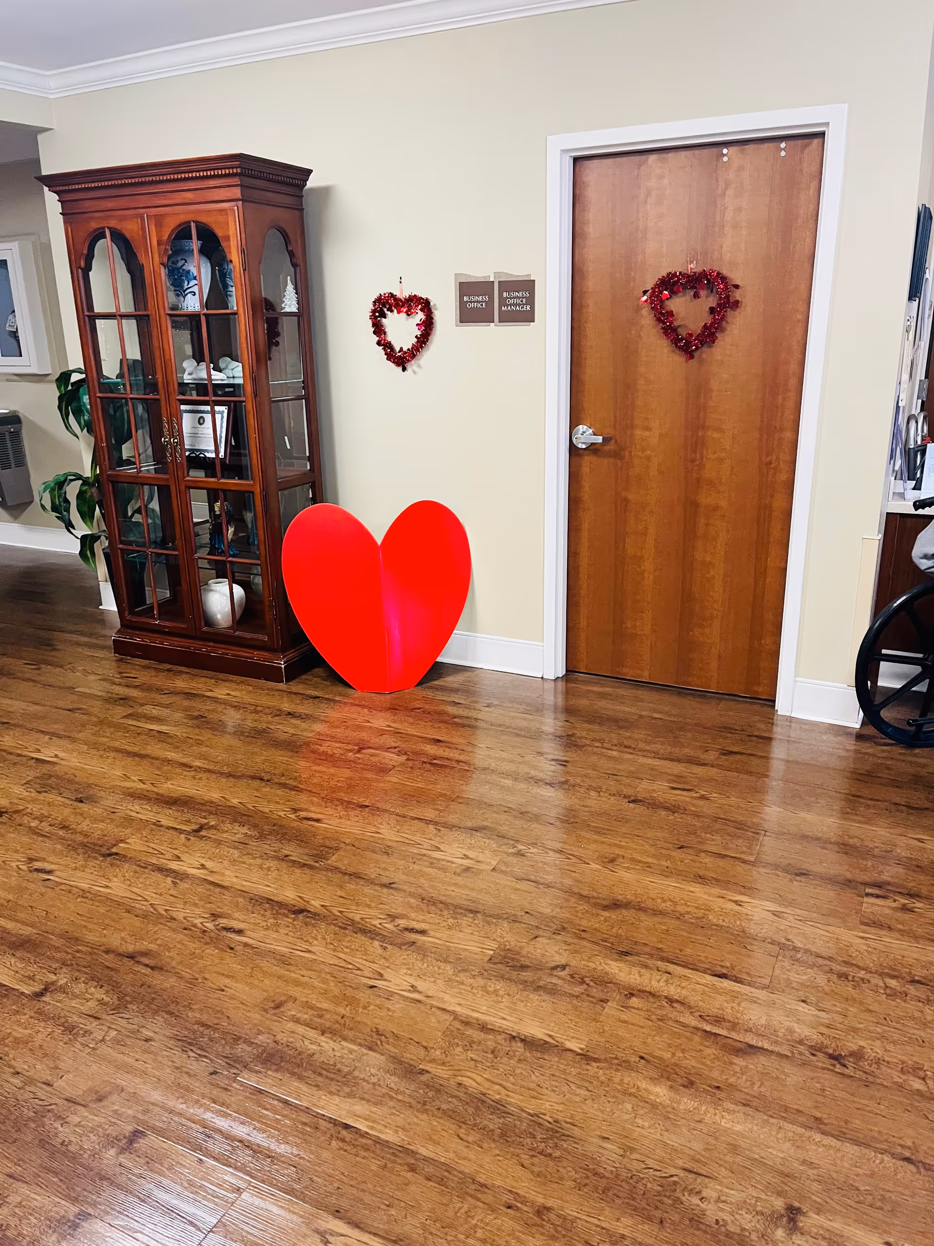 Wood-floored interior hallway with a glass-front cabinet, red heart decor, and a wooden door.
