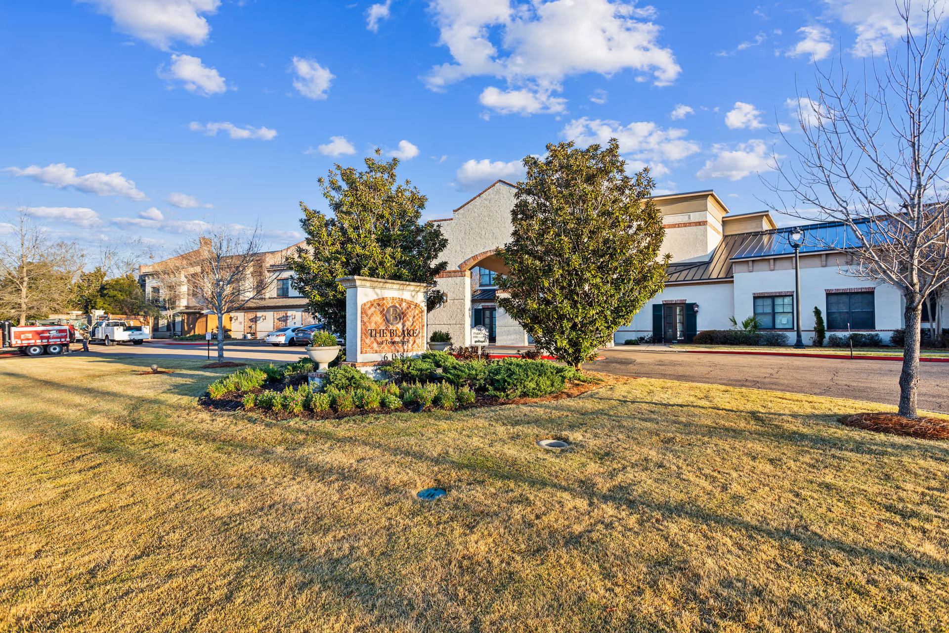 Exterior view of The Blake at Township senior living facility with a clear blue sky, manicured lawn, trees, and a sign displaying the facility's name in front of the building.