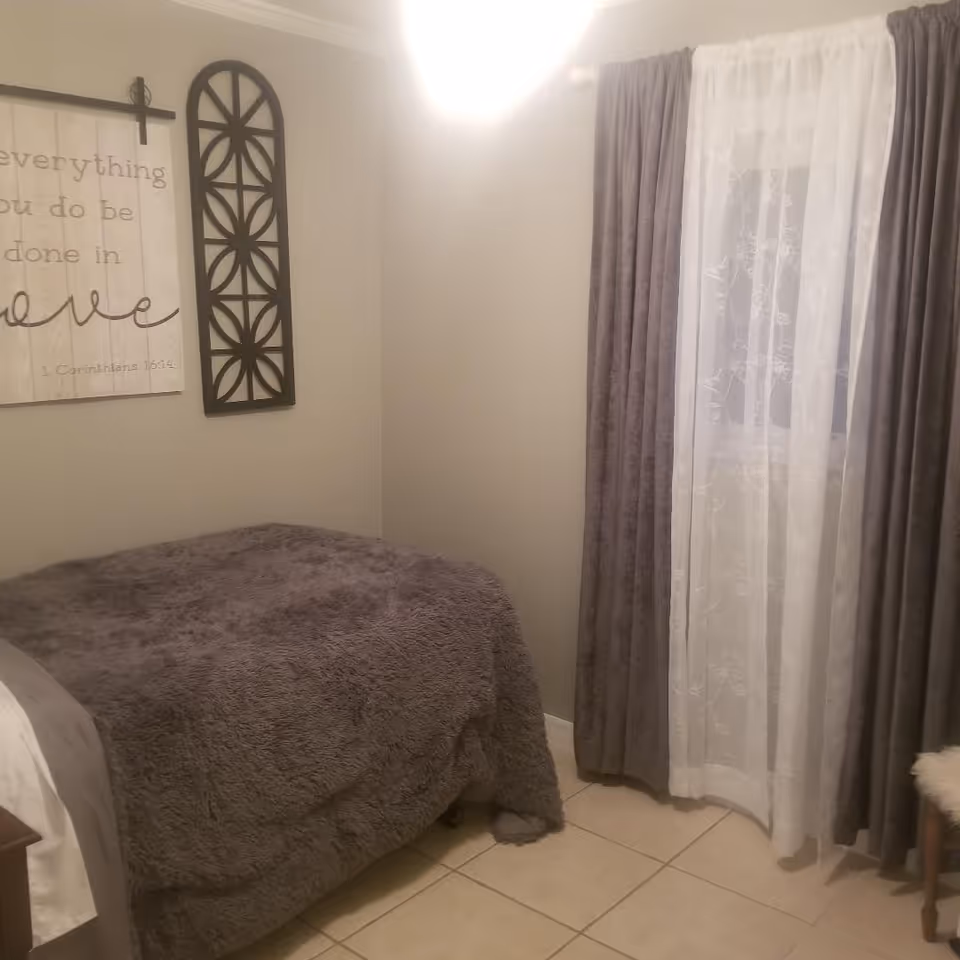 Small bedroom with a gray fuzzy bedspread, decorative wall art, and a window with sheer and gray curtains.