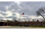 Front view of Keosauqua Health Care Center: brick building, flagpole, trees, cloudy sky.