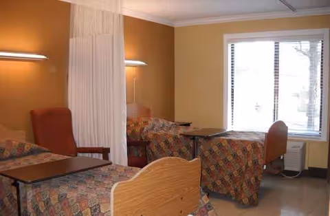 Two beds with patterned bedspreads, a curtain divider, and a desk in a shared senior room.