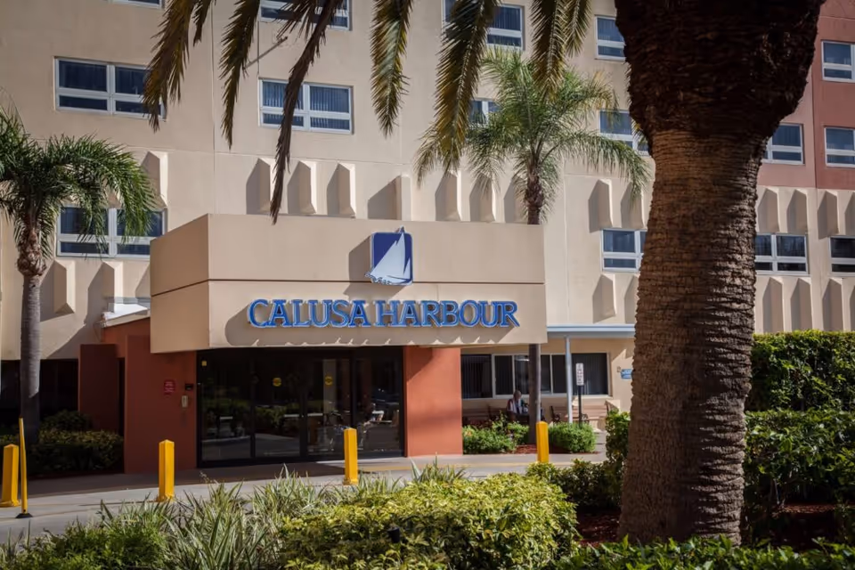 Exterior front entrance of Calusa Harbour facility with palm trees and landscaping in the foreground.