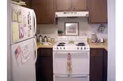 Compact kitchen with white stove, refrigerator, brown cabinets, and counter appliances.