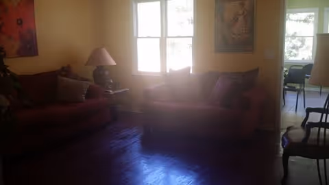 Cozy living room with red sofas, a lamp, and windows in a senior facility.