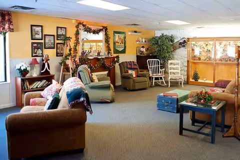 Cozy senior living lounge with multiple couches, chairs, plants, and festive decorations.