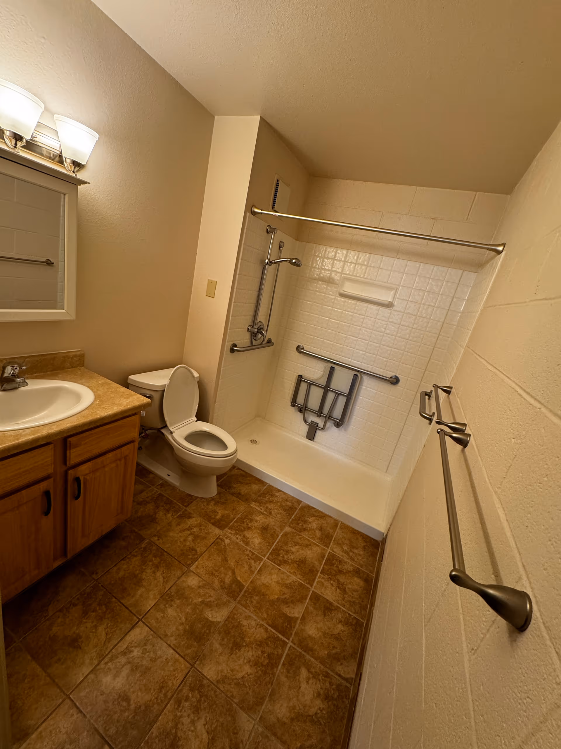 Accessible bathroom with a sink vanity, toilet, and a shower equipped with grab bars and a fold-down seat.