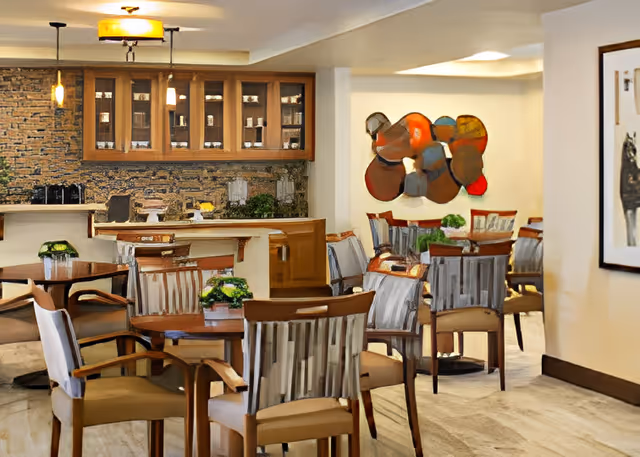 Bright dining room with wooden tables and chairs, small potted plants on the tables, a serving counter with cabinets, and abstract wall art on the far wall.
