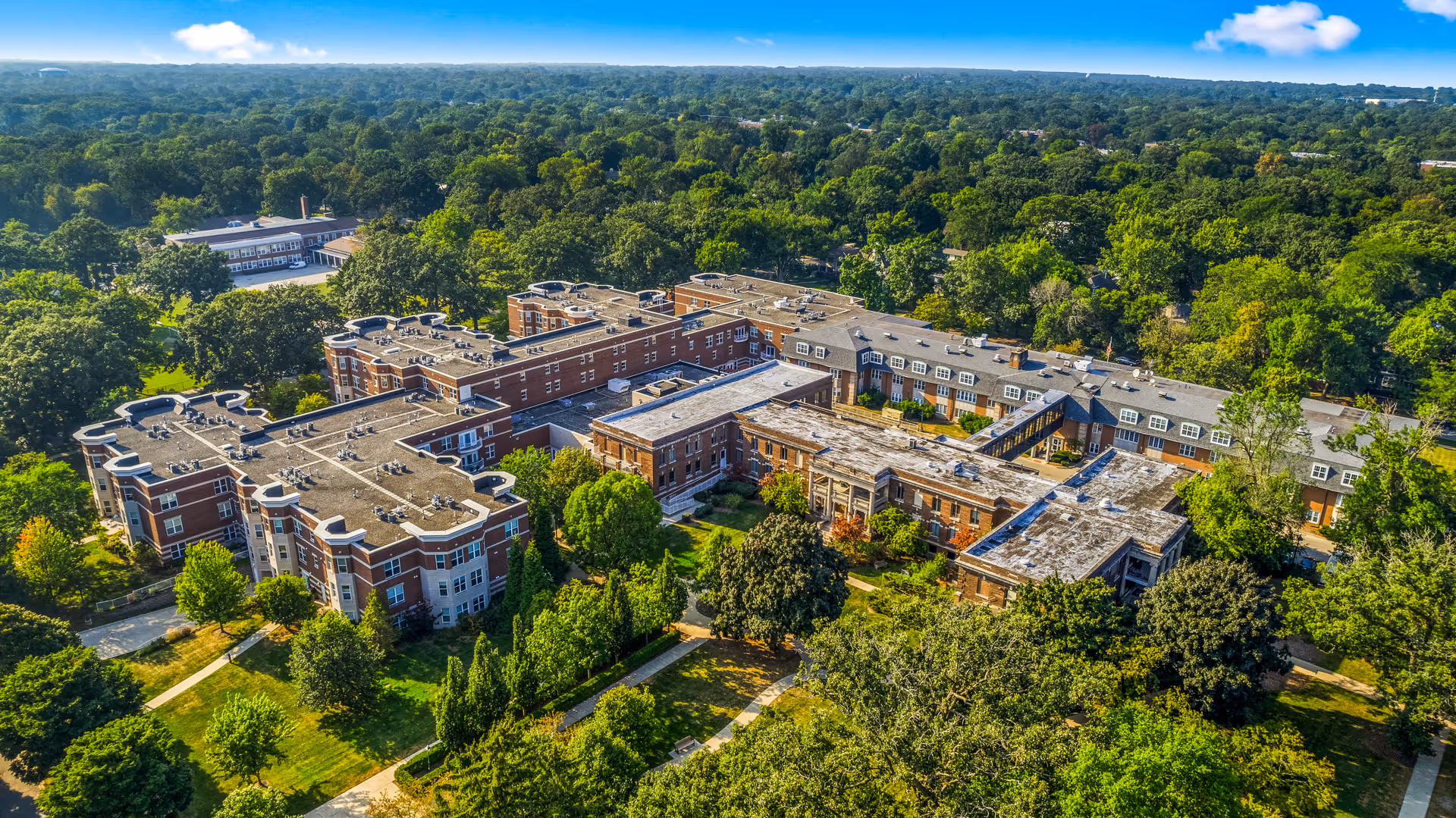 Aerial view of a large senior living facility named Three Crowns Park surrounded by dense green trees and landscaped grounds under a clear blue sky.