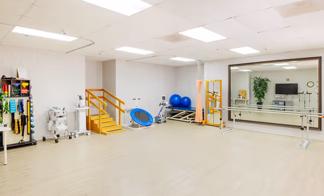 Bright rehabilitation/exercise room with a large mirror, parallel bars, small therapy stairs, exercise equipment and stability balls.