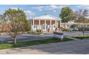 Front entrance of a single-story post-acute care facility with a white-columned portico, circular driveway, landscaping, and a brick sign.