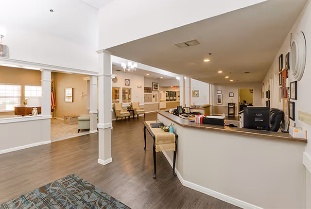 Reception area and lounge inside a senior living facility, featuring a desk, seating, and hallways.