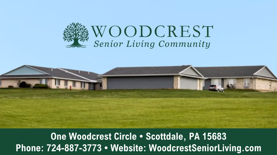 Exterior view of Woodcrest Senior Living Community buildings with a large green lawn in the foreground under a clear blue sky.