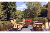 Outdoor balcony with wooden chairs, a small table, and a red flowering planter.