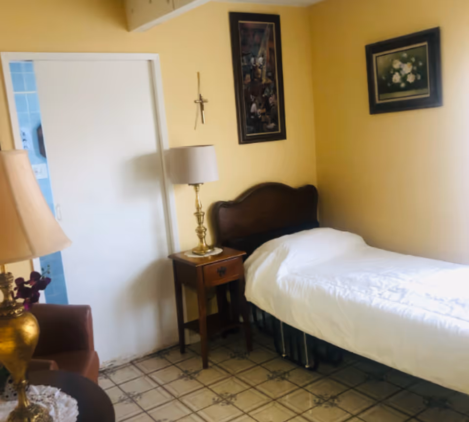 A small yellow bedroom with a single bed, nightstand, lamp, and framed art.