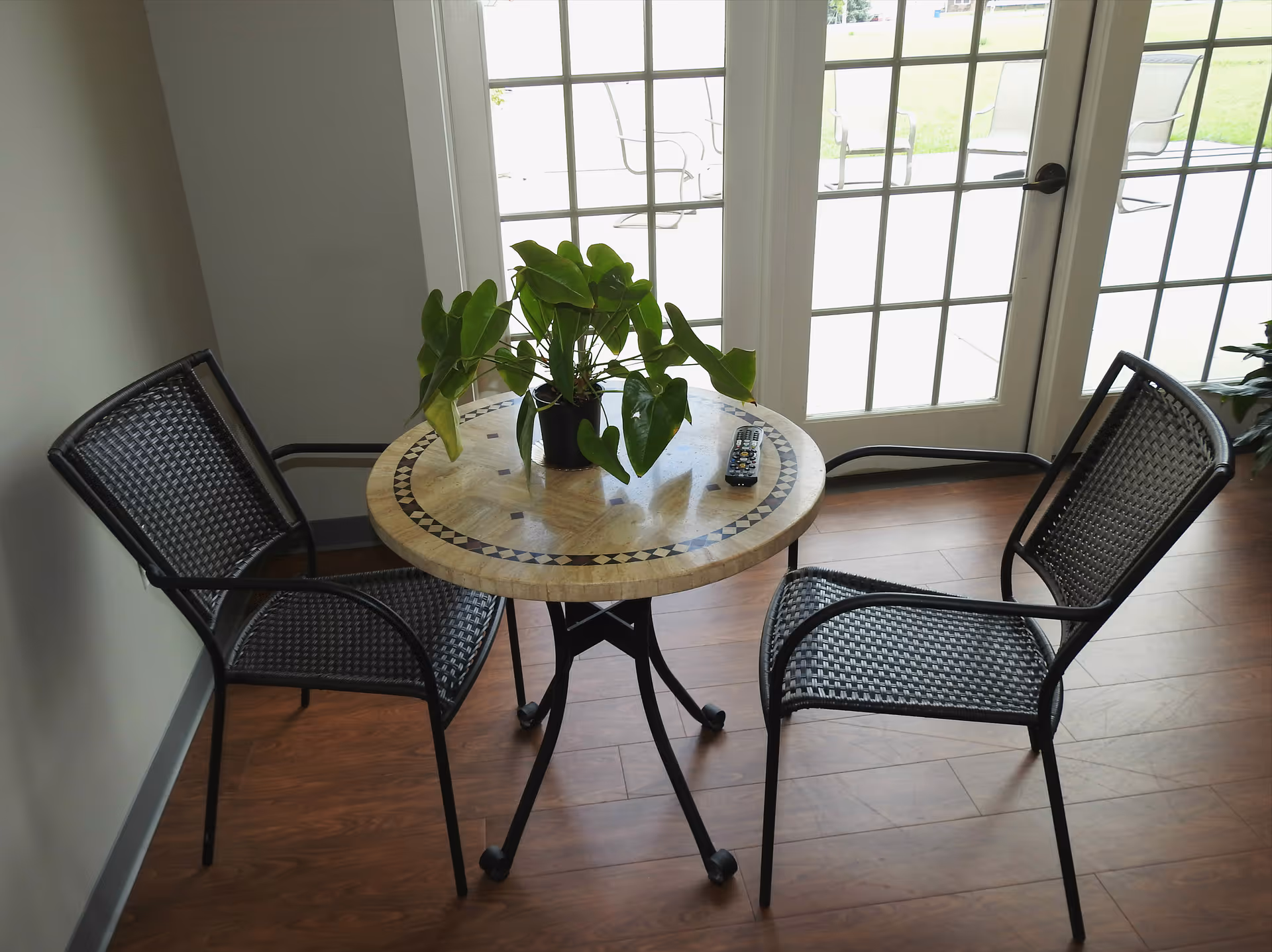 Small round table with a potted plant and a remote between two woven chairs in front of glass patio doors.