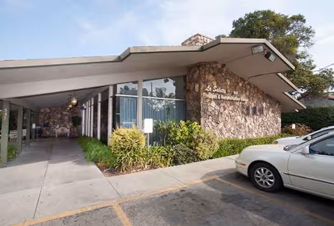 Exterior view of Fulton Gardens Post Acute facility with stone facade, entry, and a parked car.