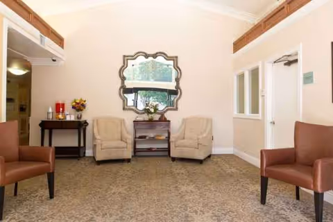 A cozy senior living lounge with armchairs, a central table, and a decorative mirror.