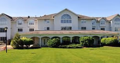 A light-colored, multi-story senior living facility with an arched front walkway and manicured lawn.