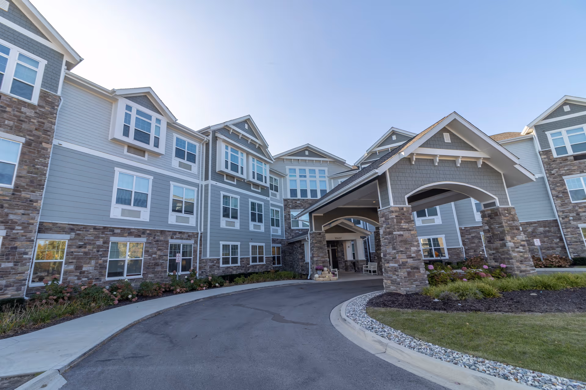 Front exterior of a multi-story senior living building with a covered porte-cochere entrance and landscaped driveway.
