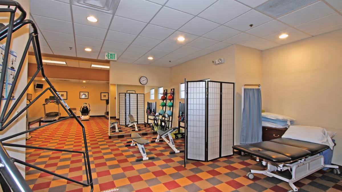 Exercise and physical therapy room with a treatment table, exercise equipment, medicine balls, and folding privacy screens.
