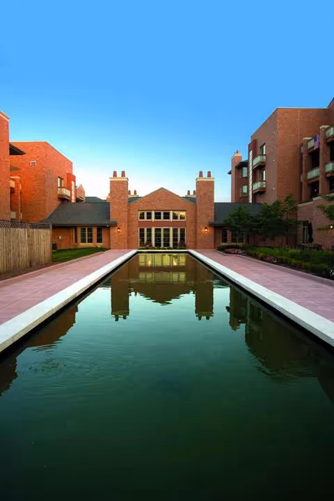 The Willows at Brooking Park's red brick buildings surround a long reflecting pool courtyard.