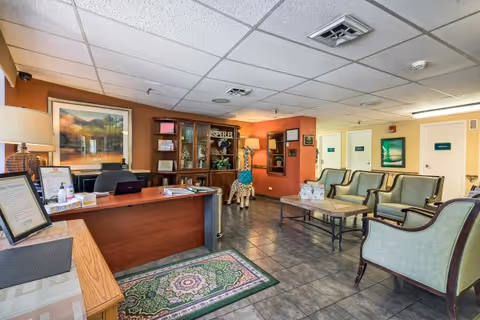 Reception area with a front desk, seating area of armchairs and a coffee table, decorative shelving and tiled floor.
