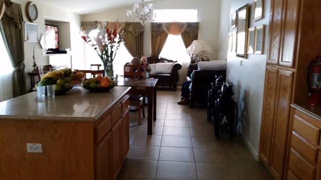 Open-concept senior living area with kitchen island, dining table, and residents relaxing in background.
