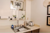 Small kitchenette sink area with a window, potted plants, paper towel, coffee maker, and toaster on the counter.