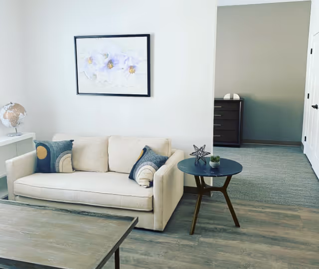 Bright living room with a beige sofa, round side table, coffee table, and floral wall art.