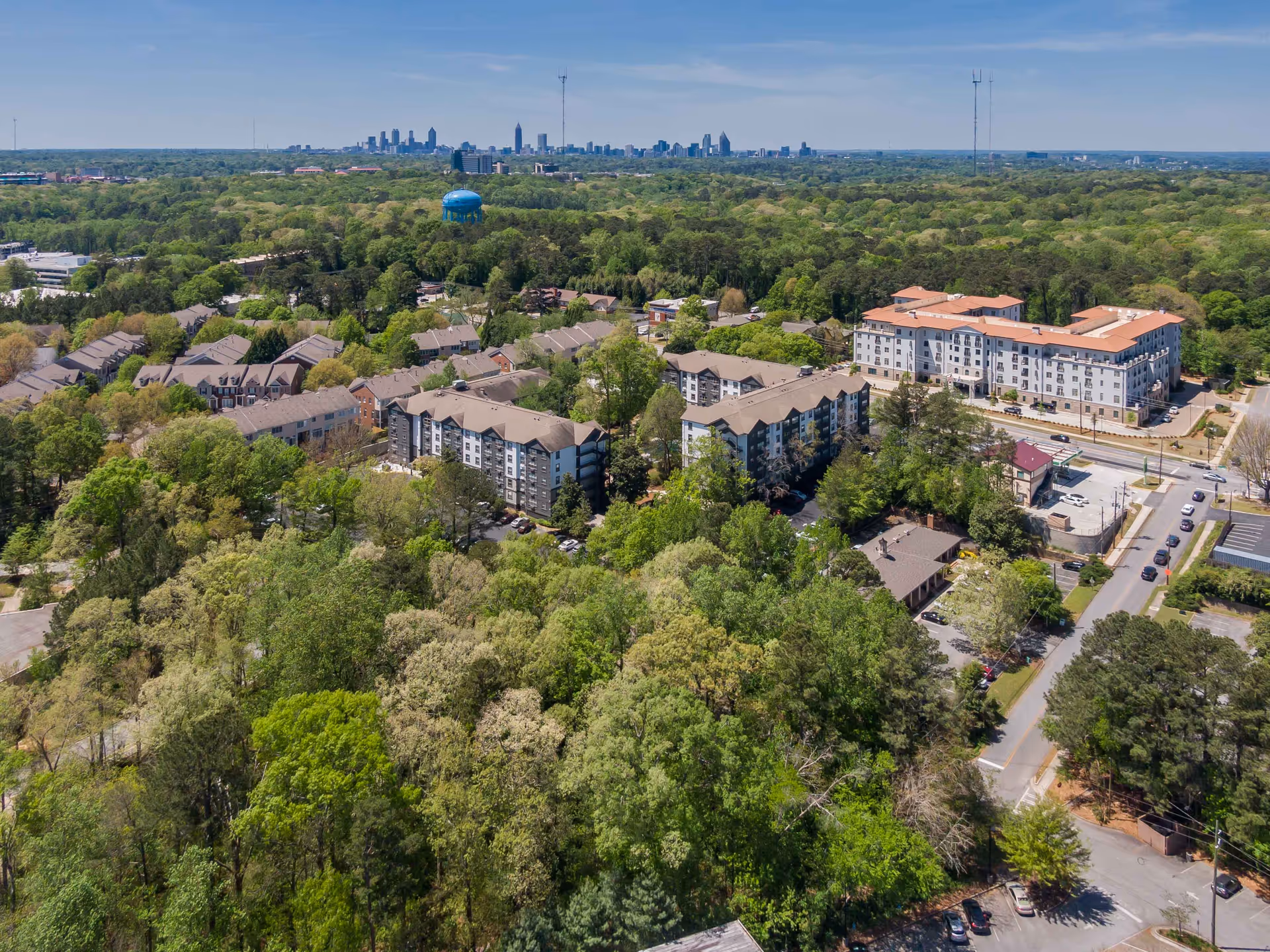 Aerial view of a senior living community with multiple apartment buildings amid dense trees and a distant city skyline.