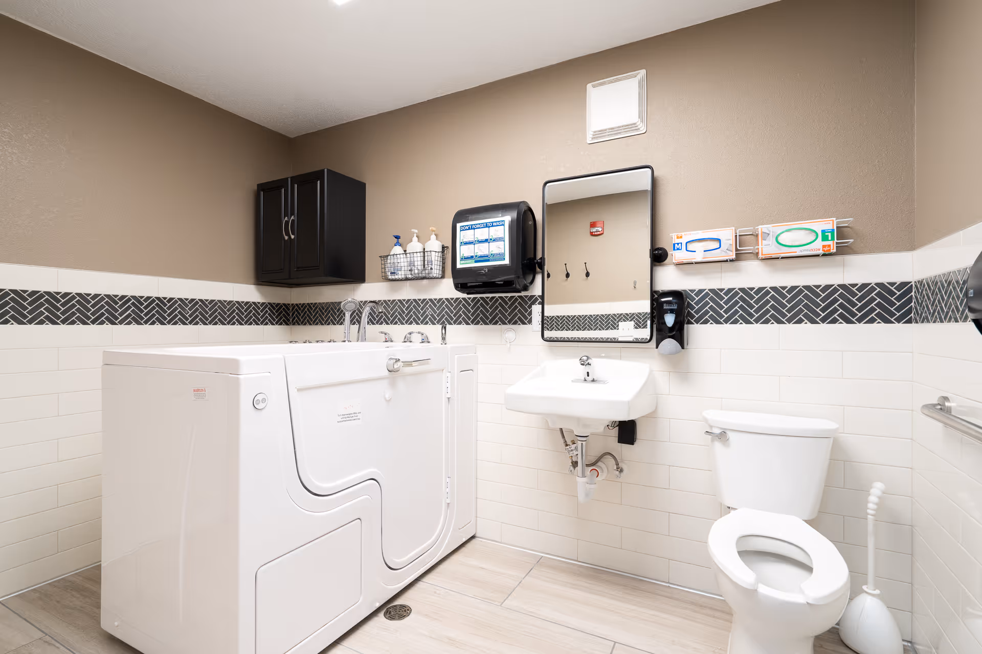 Accessible bathroom featuring a white walk-in tub, wall-mounted sink and mirror, toilet, and a storage cabinet.