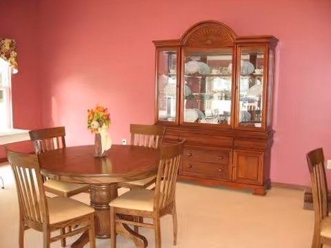 Dining room with pink walls, a round wooden table, chairs, and a china cabinet.