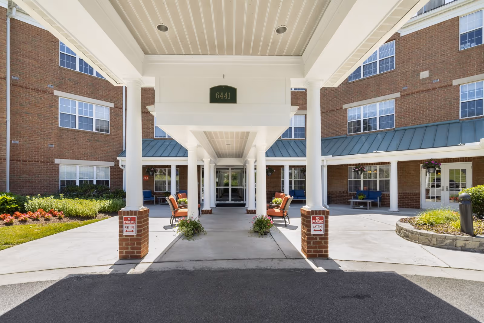 Sunlit covered entrance with white columns and seating leading into a three-story brick building labeled 6441.