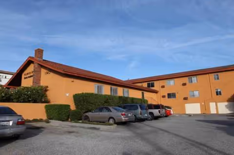 Exterior view of Hacienda Grande Senior Assisted Living building with parked cars under a blue sky.