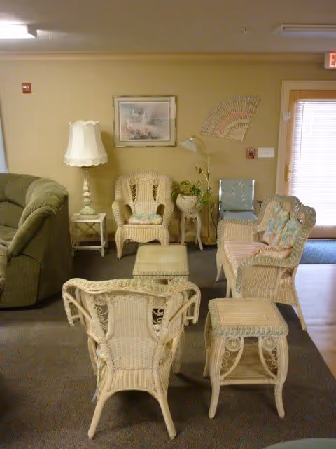 A cozy seating area with wicker chairs and stools around a small table, a sofa, lamp, framed artwork, and a door in the background.