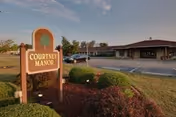 Exterior view of Courtney Manor sign with shrubs and the facility in the background.