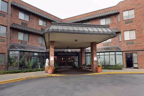 Brick senior living facility with a covered entrance and potted plants at the front