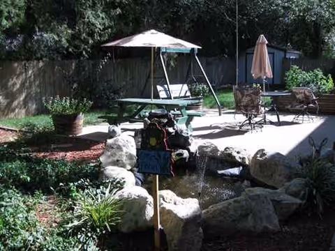 Sunny outdoor patio with a picnic table under an umbrella and a rock fountain.