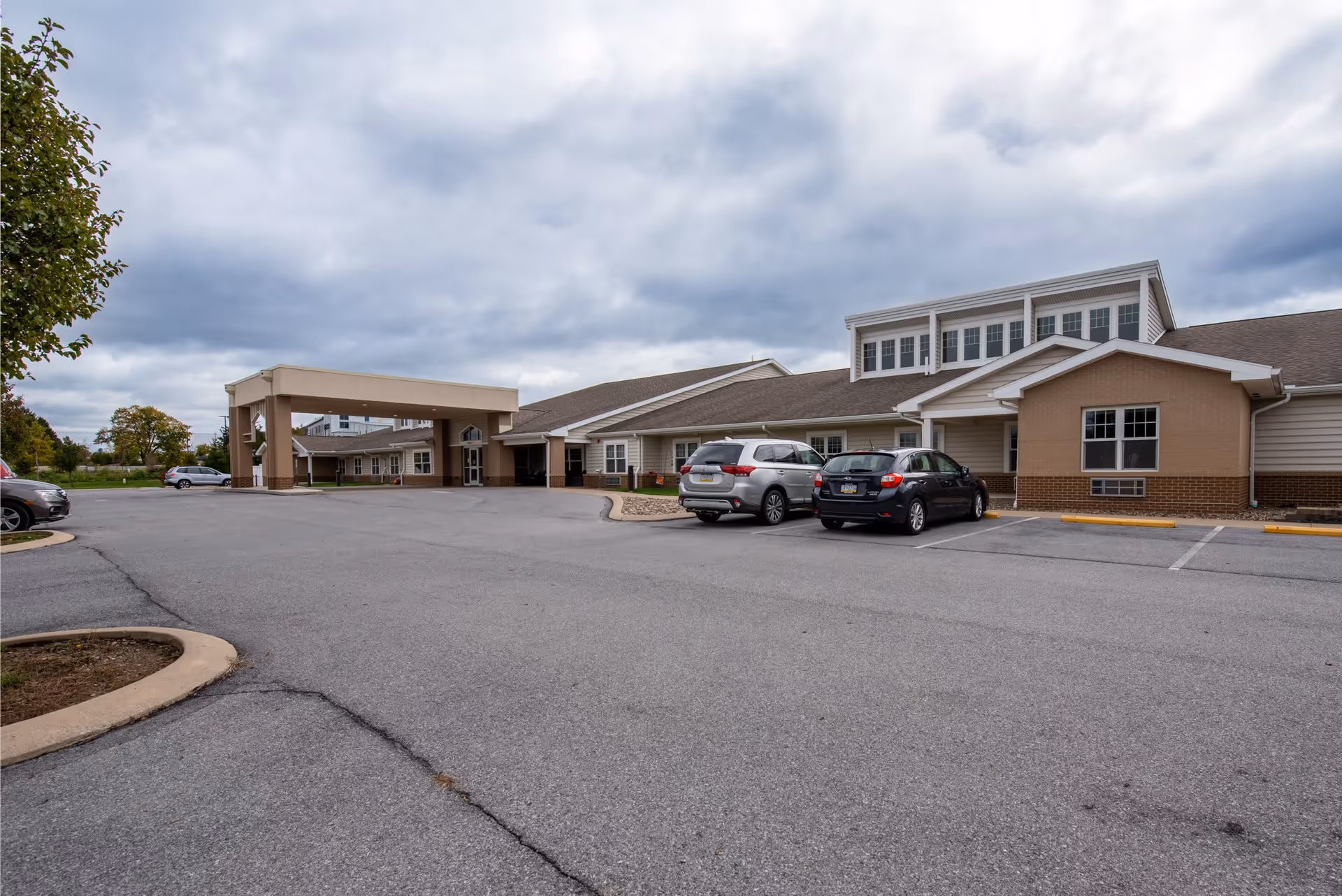 Exterior view of Wynwood House Personal Care Homes building with a covered entrance, several parked cars, and a cloudy sky overhead.