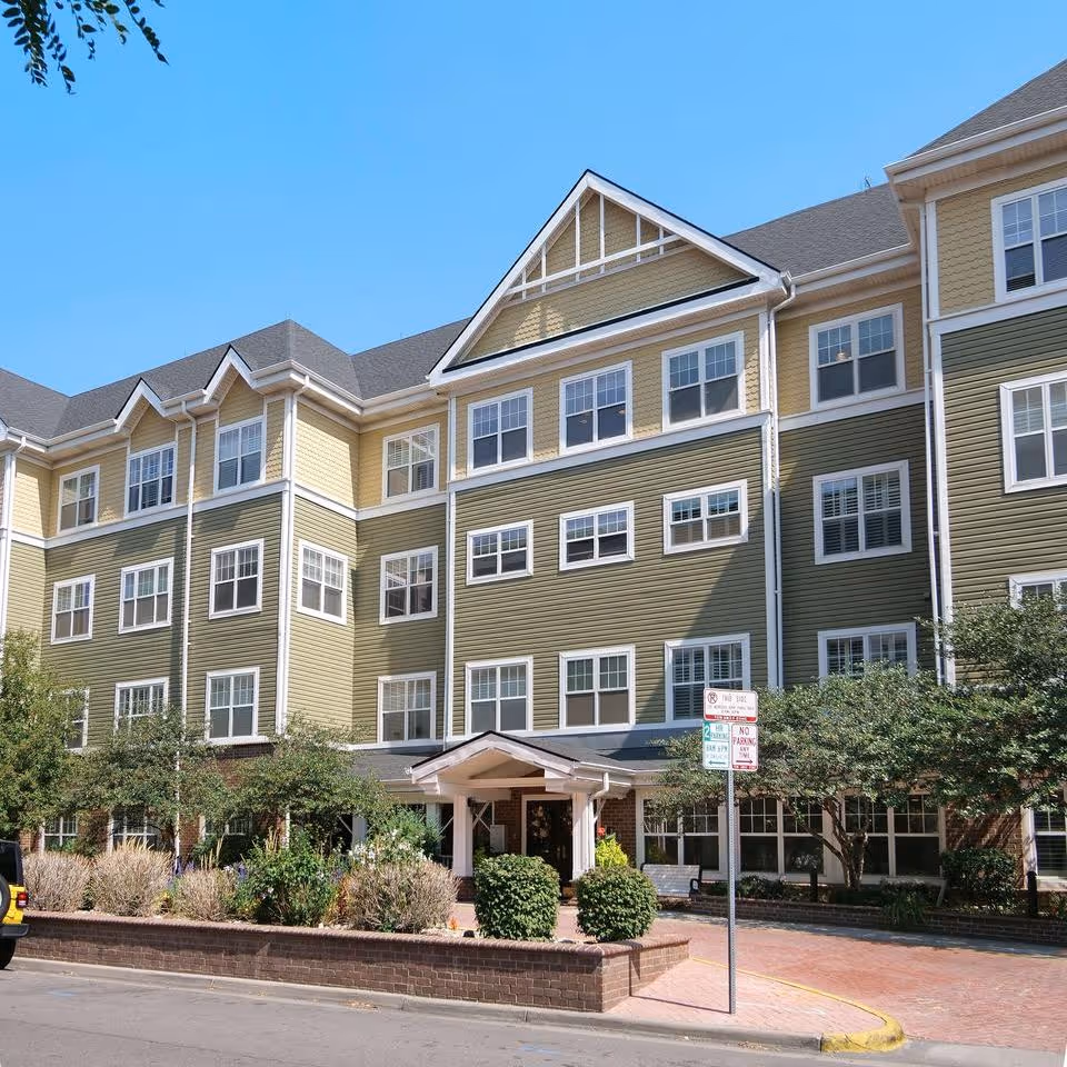 Front exterior of a multi-story building with green and yellow siding, many windows, a covered entrance, and landscaping.