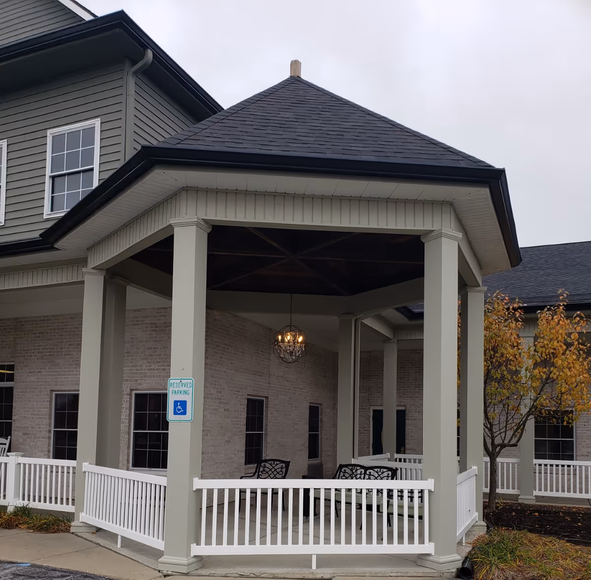 Covered front entrance/portico with columns, white railing, outdoor seating, and a hanging chandelier on a brick building.