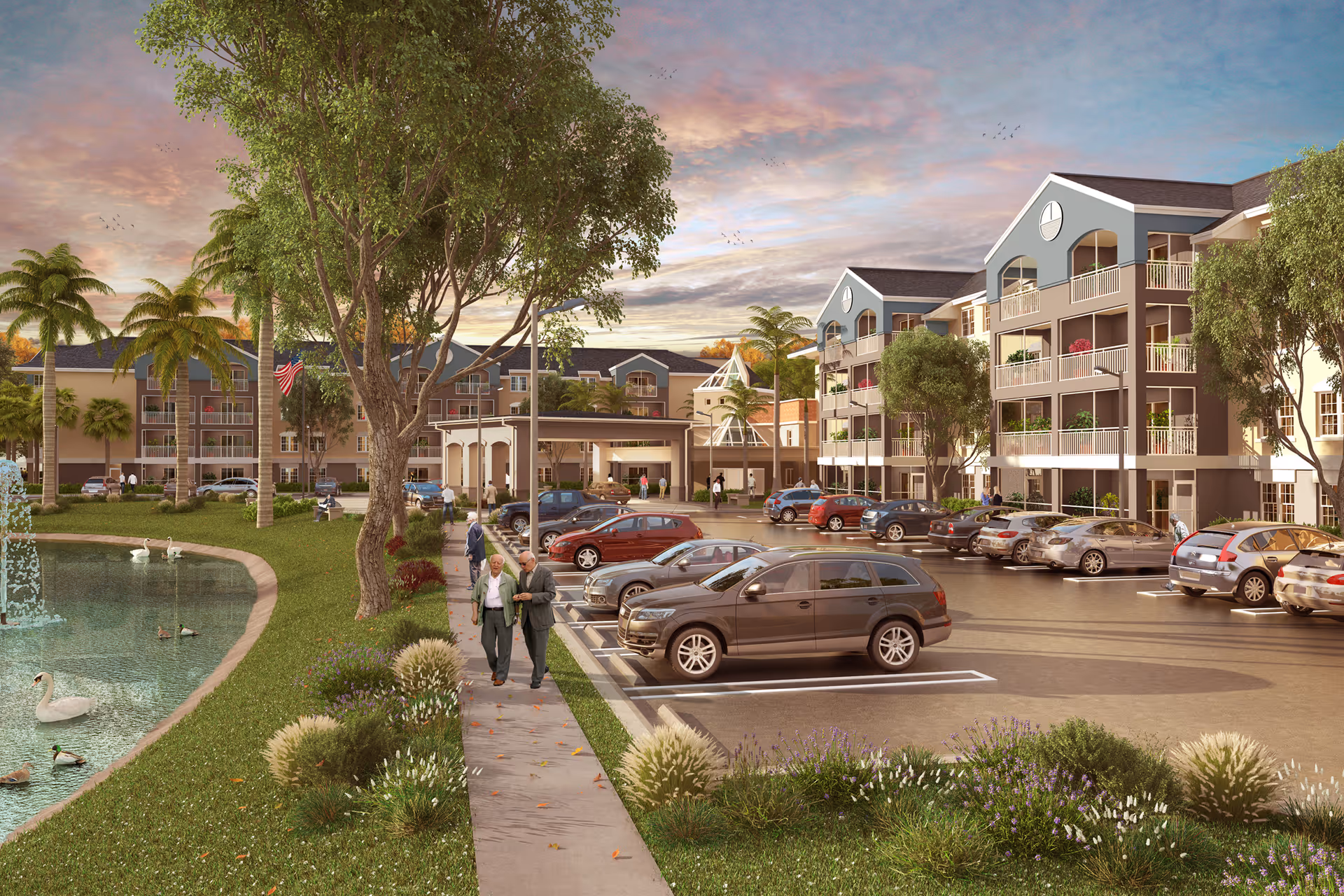 Exterior view of Discovery Village At Boynton Beach senior living facility during sunset, showing a parking lot with cars, landscaped greenery with trees and bushes, a pond with swans and ducks, and multi-story residential buildings with balconies. Two elderly people are walking on a sidewalk near the pond.