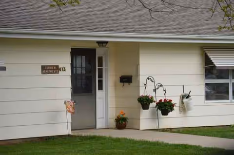 Front exterior of a single-story senior living building with hanging flower pots.