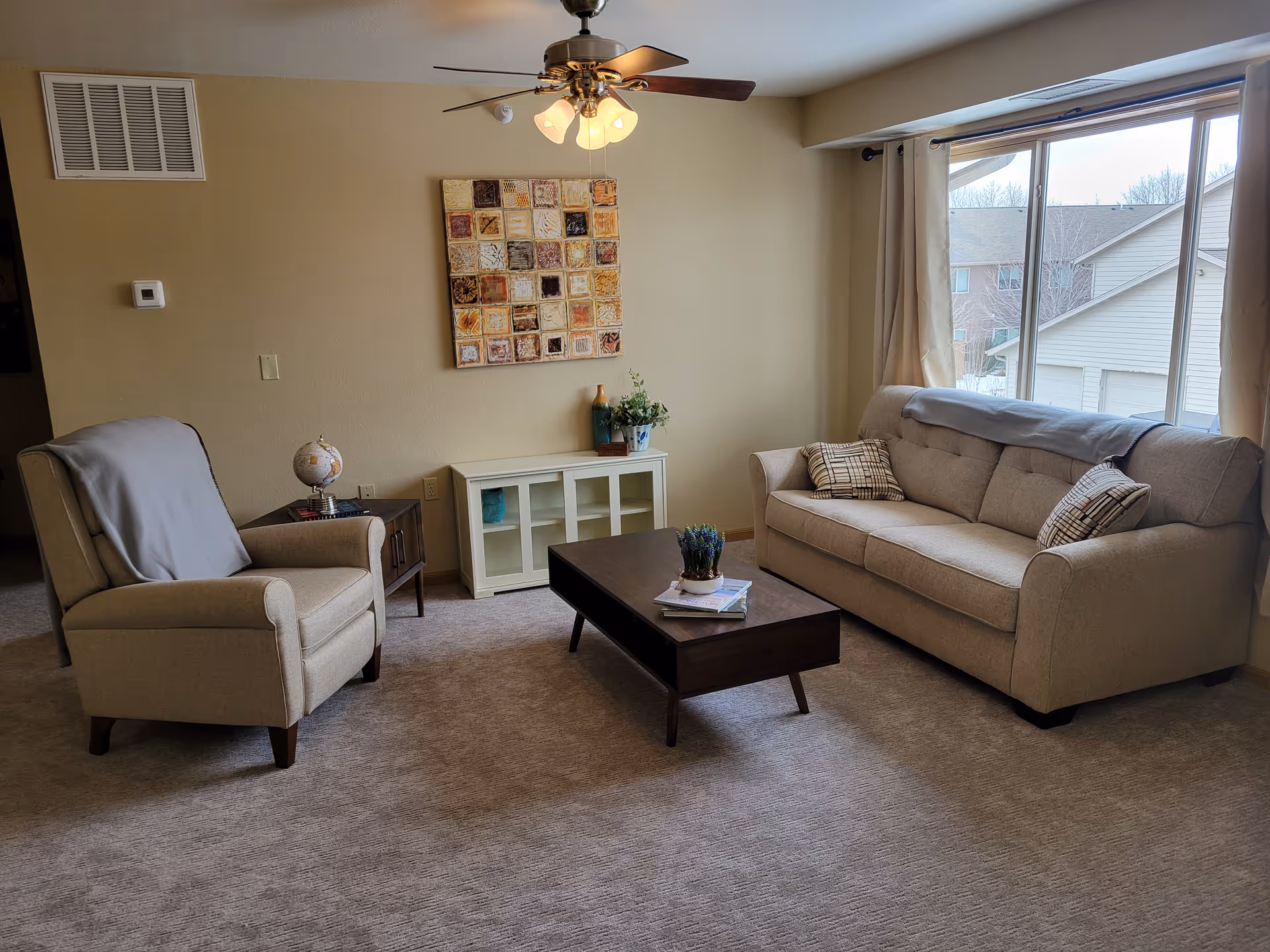Bright furnished living room with a sofa, armchair, coffee table, wall art and a large window.