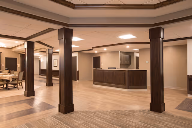 Spacious interior common area with wooden columns, a reception desk, and a dining area in the background.